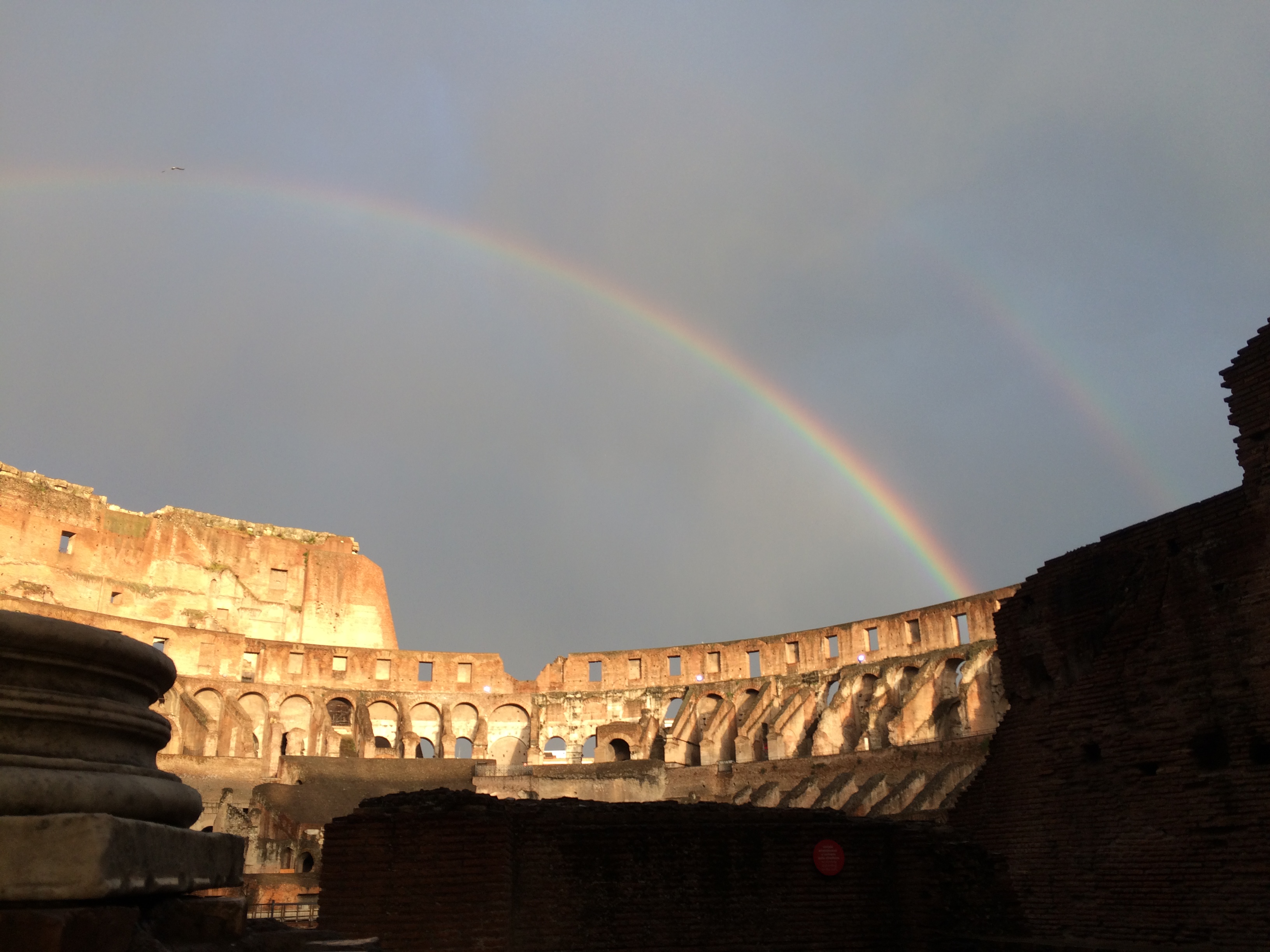 Double Rainbow above the Colosseum in Rome.  Sunshine and shadow in the foreground.  Cloud vapour streaking the sky.